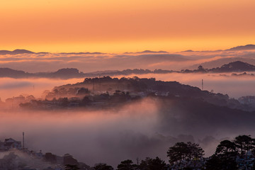 Obraz premium Mountains in fog at beautiful morning in autumn in Dalat city, Vietnam. Landscape with Langbiang mountain valley, low clouds, forest, colorful sky , city illumination at dusk.