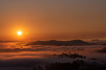 Obraz premium Mountains in fog at beautiful morning in autumn in Dalat city, Vietnam. Landscape with Langbiang mountain valley, low clouds, forest, colorful sky , city illumination at dusk.