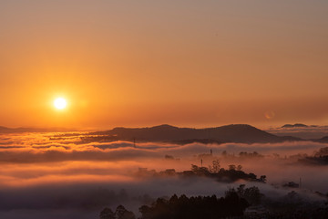 Fototapeta na wymiar Mountains in fog at beautiful morning in autumn in Dalat city, Vietnam. Landscape with Langbiang mountain valley, low clouds, forest, colorful sky , city illumination at dusk.