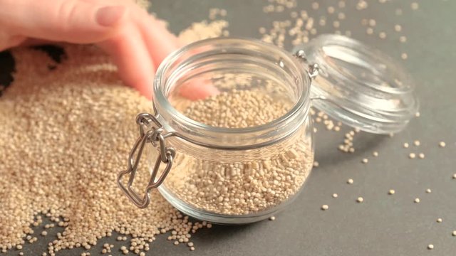 White raw quinoa, South American grain, female hands pour seeds into glass jar. Healthy and gluten free food.