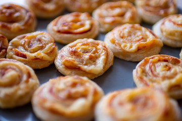 Freshly baked, crispy, salty snails from puff pastry with ham and cheese in the oven