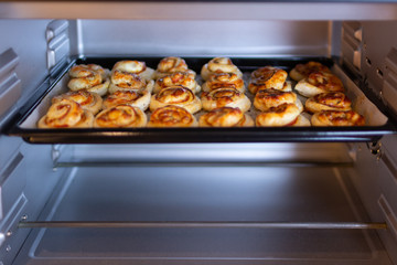Freshly baked, crispy, salty snails from puff pastry with ham and cheese in the oven