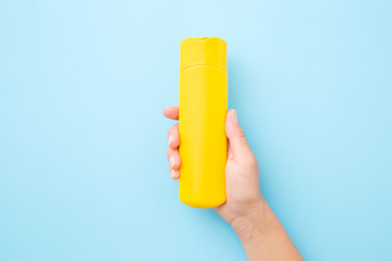 Young woman hand holding and showing yellow tube of sunscreen on light blue table background. Pastel color. Care about skin protection in hot summer. Empty place for text or logo. Closeup. Top view.