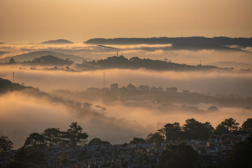 Mountains in fog at beautiful morning in autumn in Dalat city, Vietnam. Landscape with Langbiang mountain valley, low clouds, forest, colorful sky , city illumination at dusk.