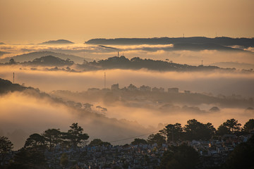 Mountains in fog at beautiful morning in autumn in Dalat city, Vietnam. Landscape with Langbiang mountain valley, low clouds, forest, colorful sky , city illumination at dusk.