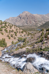 The beautiful mountain trekking road with clear blue sky and rocky hills and fresh mountain stream in Fann mountains in Tajikistan