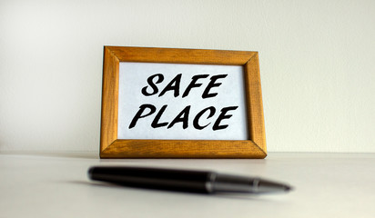 Wooden picture frame with inscription 'safe place' on beautiful white background. Pen on the table. Concept.