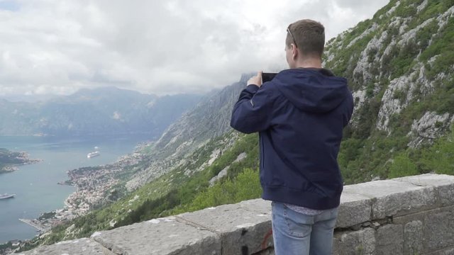 Male traveler with smartphone shooting video in beautiful place: mountains and sea view, cloudy sky. Sunny day in summer spring time. Slow motion