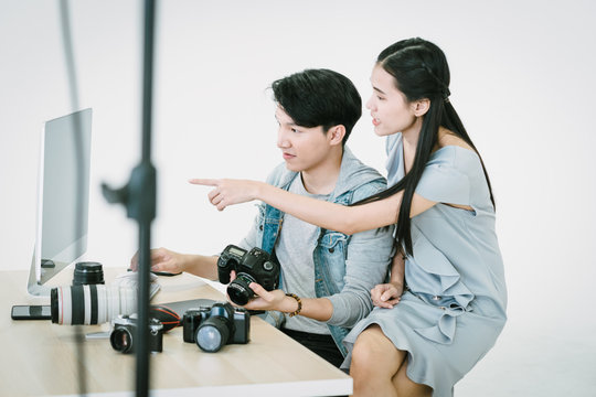 An Asian photographer and an Asian model are looking at pictures taken on a computer monitor, in a photo studio after the work is done.Review and check the quality of the photos,
