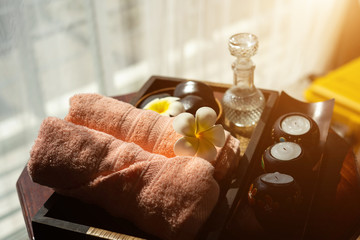 Fototapeta na wymiar Spa accessories wellness setting with pink pastel towel, cosmetic bottles, aroma oil, white plumeria flower in tray, massage stones in wooden bowl and spa candle, spa concept, copy space.