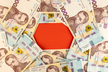 Red paper under a background of 1000 UAH or Ukrainian Hryvnia banknotes. Financial setup for mock-ups with your identity.