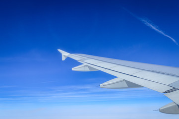 View over the clouds from the porthole of an airplane with plane wing and blue sky