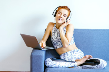 Young caucasian woman wearing sportswear, feeling smile, relax and happy while listening to online music from headset and using laptop to work from home during COVID-19, exercise to release a stress