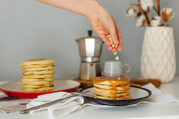 Girl pouring peanuts on pancakes near coffee maker. Morning breakfast at home in quarantine. Recipe of homemade delicious pancakes.
