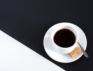 A Cup of coffee with two sugar cubes on a black and white background