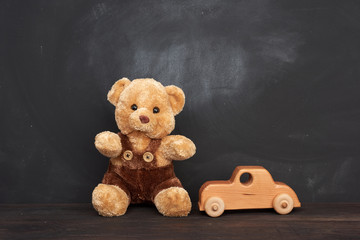 brown teddy bear sits on a brown wooden table and wooden car