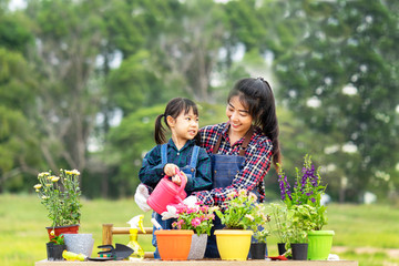 Young Asian family planting floral outdoor, a mother is coaching daughter to take care of flowers and water the plant in summer. Kids holding watering can in hands to assist her mom with smiling face.