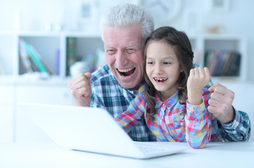 Emotional senior man with granddaughter using laptop at home