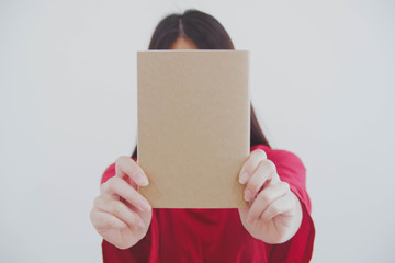 Image of a woman holding a blank brown book out to the front. White background and red shirt.