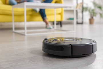 Cropped view of mother with daughter on sofa and robotic vacuum cleaner on floor in living room