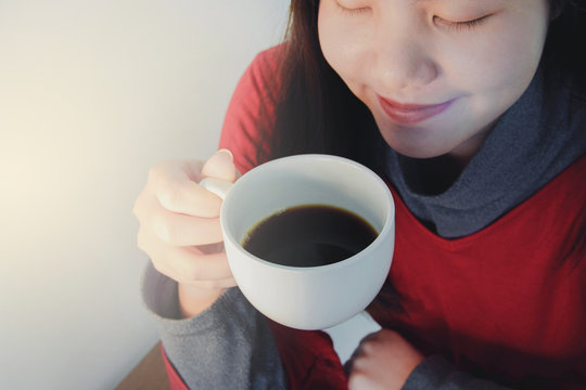 Image of an asian woman sipping a hot cup of coffee with white flare.