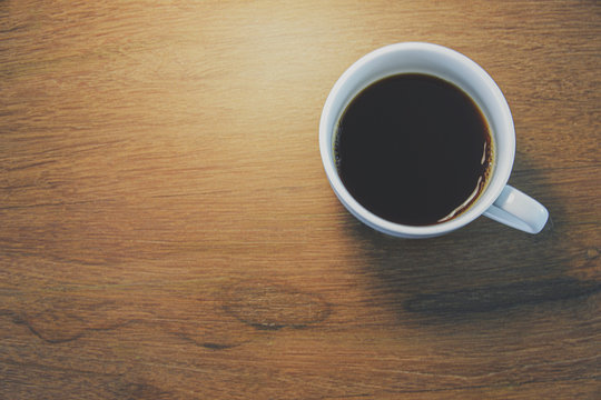 Closed up image of hands holding a cup of coffee with background of wood table.