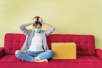 Young woman feeling disheartened with box on red couch in living room because of losing job, entrepreneurs layoff employee to reduce cost. Business impact from Coronavirus COVID-19 pandemic disease