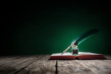 Quill pen and inkwell on old book background with copy space