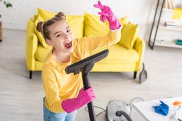 High angle view of cute child singing with vacuum cleaner and showing rock sign in living room