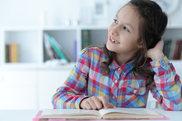 Cute schoolgirl sitting at table at home