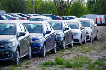 Identical blue cars stand in a row in a Parking lot or market for sale. View of the side mirrors,...