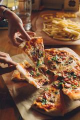 eating delicious vegitable and meat pizza and french fries and chilling with friends in the cozy cafe. Pizza on the wooden table. Grabbing slices of pizza by hands. Junk food.