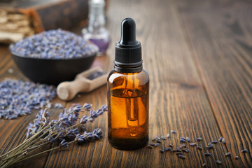 Dropper bottle of essential lavender oil. Bowl of dry lavender flowers on background.