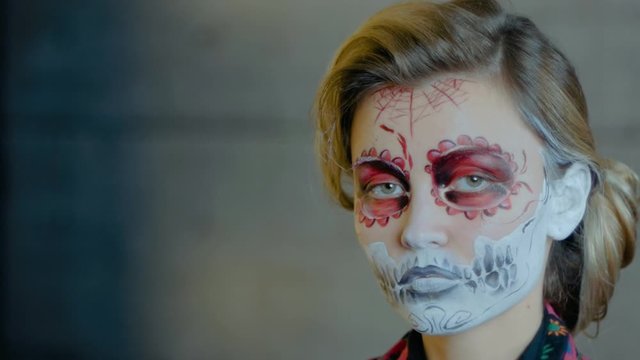 Nice girl with body art tattoo patterned skull chicano style on her face looking at the camera. Halloween party and mexicans death day santa muerte concept