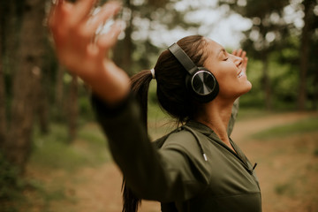 Young woman with earphones preading her arms in the forest because she enjoys training outside