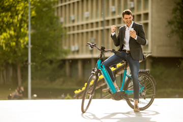 Young businessman on the ebike received gret news by mobile phone