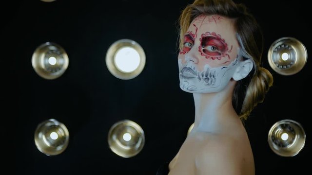 Nice girl with body art tattoo patterned skull chicano style on her face looking at the camera. Halloween party and mexicans death day santa muerte concept