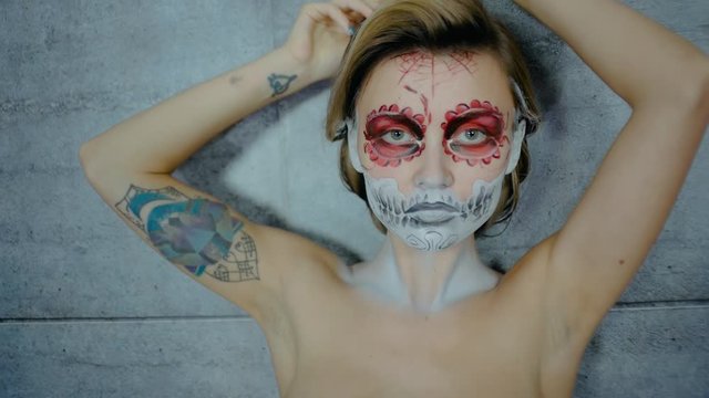 Nice girl with body art tattoo patterned skull chicano style on her face looking at the camera. Halloween party and mexicans death day santa muerte concept