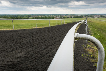Deep depth of field of white track barriers seen extending to the far distance. The track is used for horse gallops, the track showing its soft texture. - obrazy, fototapety, plakaty