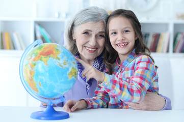 Smiling grandmother and granddaughter sitting at table with globe