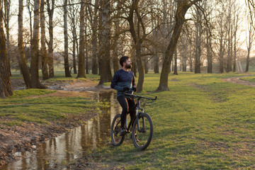 Naklejka premium Cyclist in shorts and jersey on a modern carbon hardtail bike with an air suspension fork standing on a cliff against the background of fresh green spring forest