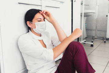 Young female asleep surgery nurse has headache and sitting down in clinic. Burnout of nurses. Viral...