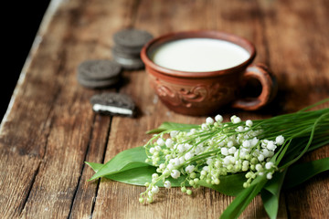 On a wooden table is a cup with milk and chocolate cookies.

