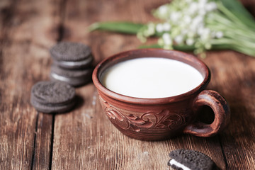 On a wooden table is a cup with milk and chocolate cookies.
