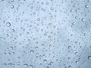 Raindrops on a transparent glass against a cloudy blue sky. Condensation and precipitation concept.