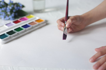 Children's hand holds a brush and paints.
