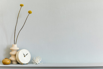 Minimalistic composition on the shelf with dried flower in design vase, white clock and accessories. Grey wall. Copy space.