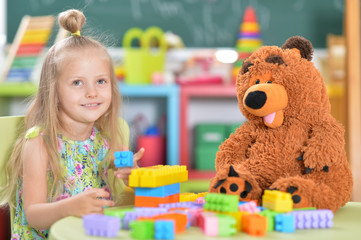 Little girl playing with teddy bear and colorful plastic blocks