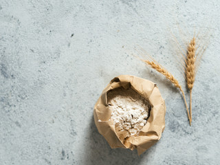 Wheat flour in paper bag and spikes over gray cement background. Food and baking ingredient - all-purpose flour with copy space