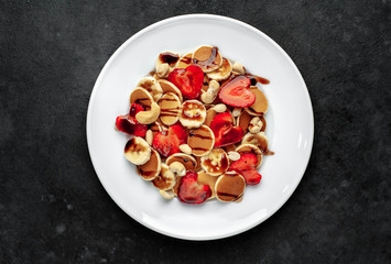 Mini pancakes with strawberries, bananas, nuts in a plate on a stone background. delicious breakfast concept